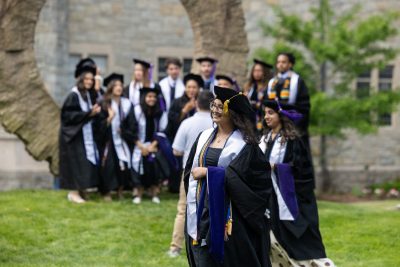 Graduates stand in front of U shaped stone statue