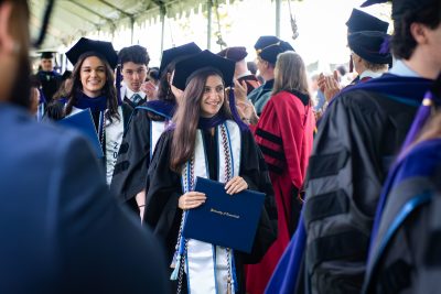 Graduates hold diplomas and walk through professors cheering for them